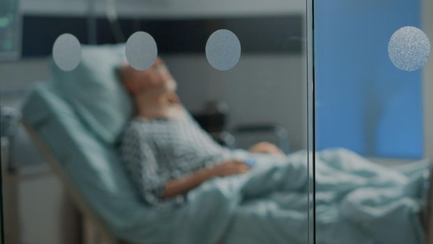 Sick old man laying in hospital ward bed with cervical neck collar at medical facility. Elder patient sitting in intensive care room waiting for surgery diagnosis from doctor to start treatment