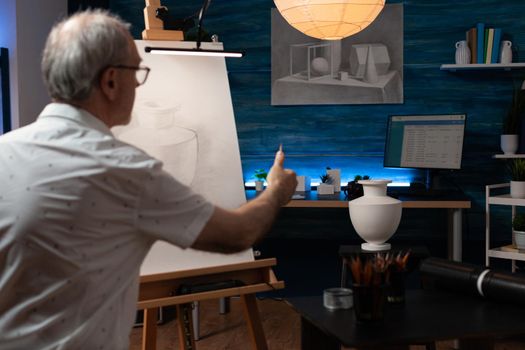 Senior artist using vase for drawing inspiration on canvas in workshop space. Caucasian elder man working on authentic masterpiece with professional instruments in artwork studio
