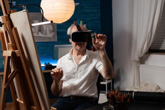 Aged adult with vr glasses seeking inspiration for realistic drawing in workspace at home. Elder artist using headset with virtual reality technology for masterpiece. Old man with artistic vision