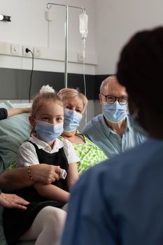 African american nurse monitoring elderly senior woman after clinical surgery in hospital ward. Caring family wearing medical face mask against covid19 while visiting patient during recovery