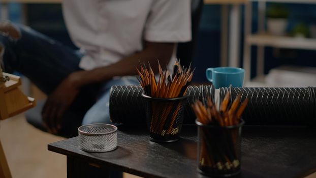 Close up of art tools and colorful pencils on workshop table in studio at home. African american person working on canvas drawing using modern instruments for masterpiece concept