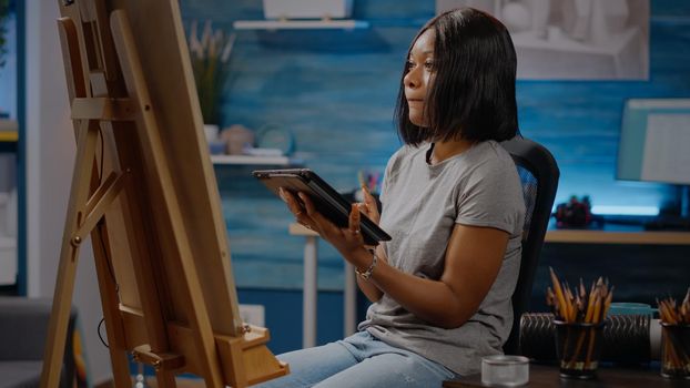 Black young artist using digital tablet for drawing design in art studio space. African american woman with modern technology working on canvas for fine art and authentic masterpiece
