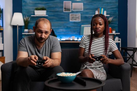 POV of interracial couple playing video game on console holding joysticks at television. Multi ethnic partners looking at camera while enjoying fun activity with technology and controllers