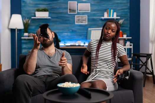 Interracial couple feeling sad after losing at video game. Multi ethnic partners playing with controllers and console on television. Mixed race people with fun play and joysticks