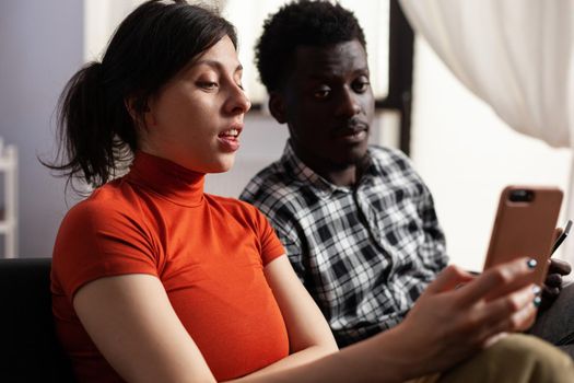 Close up of modern interracial couple using smartphones at home. Multi ethnic partners holding digital devices with technology. Mixed race people having gadgets with online internet.