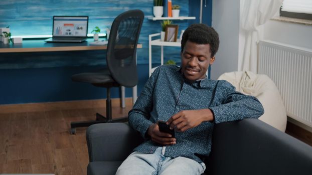 African american man with phone in hands looking at online streaming services content, enjoying working from home, connection via internet web services. Home technology user