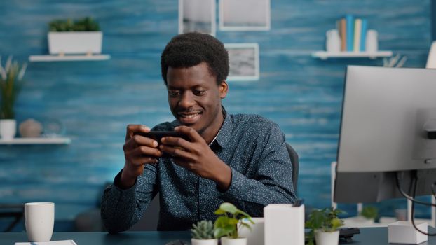 African american man playing video games on his phone, smiling and enjoying leisure time. Mobile entertainment gaming session, using online internet web video games app