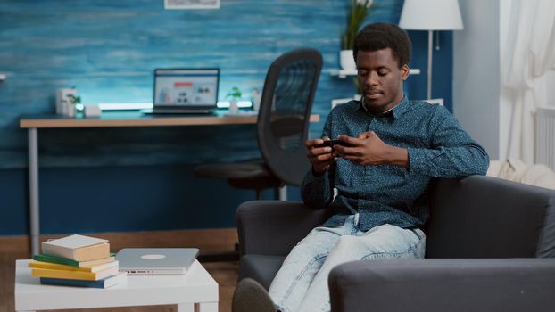 Exhausted african american man falling asleep while holding phone in his hands, overworked manager overburdened black freelancer in home office working from home. Overwhelmed guy closing eyes