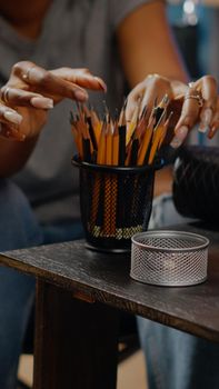 Close up of art tools and pencils on table in artwork space at home. Disabled african american artist with handicap sitting in wheelchair drawing authentic masterpiece in background