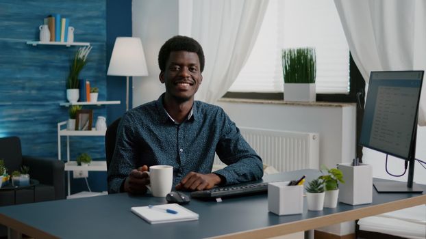 Zoom in portrait shot of african american black man freelancer smiling to camera, handsome young man in modern flat apartment. Happy attractive male of african ethnicity. Slow motion shot