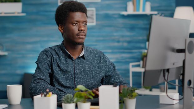 Closeup portrait of black african american man working on computer in living room, smiling at camera. Remote internet online web manager working from home keeping social distance