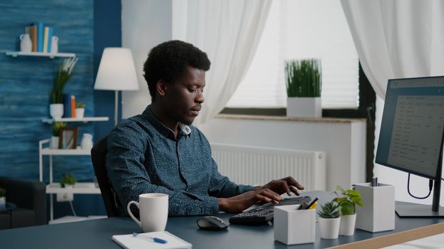 Confident remote african american black man worker doing his job from home, taking a sip of coffee, working from home. African ethnicity computer user in modern flat. Internet online browsing and communication