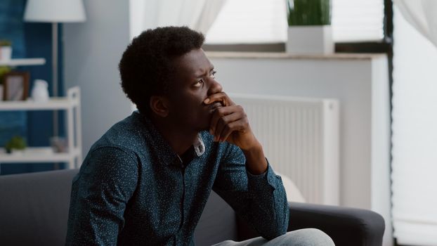 Portrait of pensive thoughtful authentic african american man looking out the window, dreaming or thinking at problems. Adult black man in living room from home office