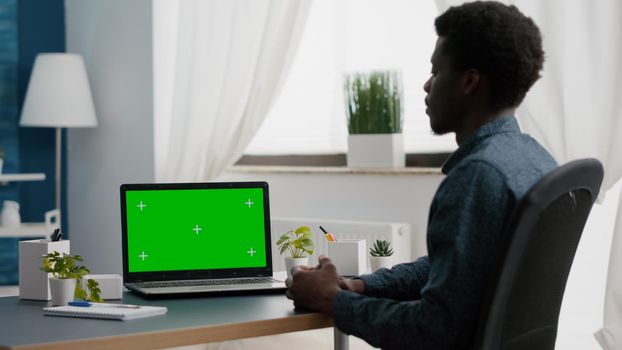 Isolated mock up display on laptop in bright living room. African american man working from home on green screen mockup chroma key display ready and easily replaceable