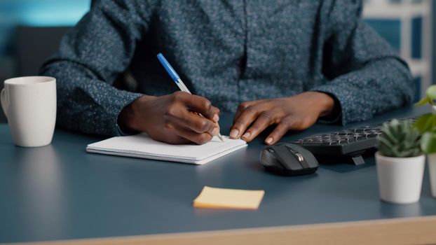 Closeup african american black man hands taking notes on notepad using a pen. Male adult hands of remote worker writing text on white paper. Business student in home office handwriting documents