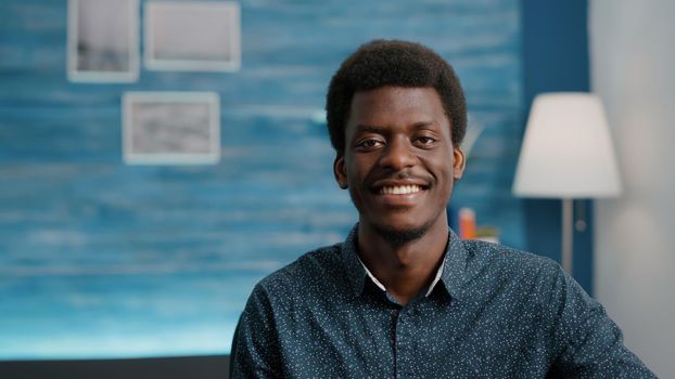 Close up portrait of charming handsome african american man smiling to camera, young black man in cozy modern flat apartment. Happy succesful attractive freelancer of african ethnicity. Slow motion shot