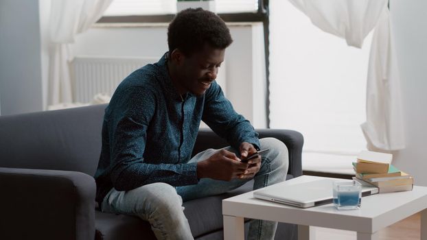 Positive authentic black african american man smiling while using a smartphone to browse and check social media status. Remote working guy taking a break, using phone for relaxation