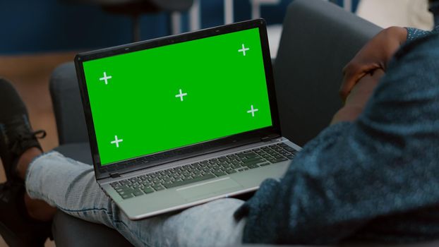 Close up of mock up green screen laptop display in african american guy laps, sitting in bed in living room. Isolated mockup template ready for easy replacement