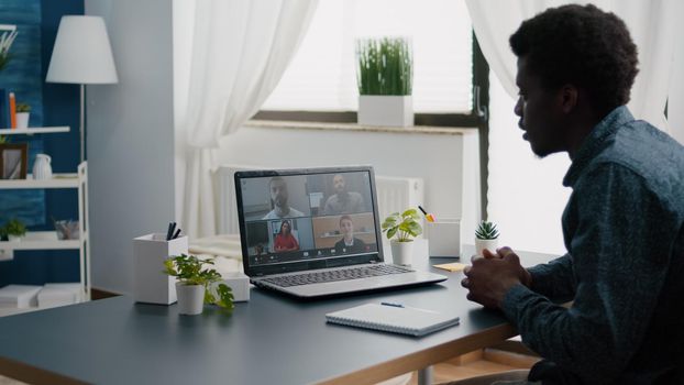 Black man remote worker working from home taking online office call with partners and colleagues, greeting them. Computer user from home office on video internet conference via webcam conference call