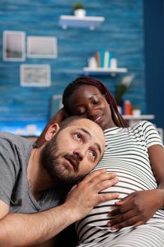 Close up of caucasian father of child placing head and hand on belly of black pregnant woman. Interracial couple with pregnancy smiling and bonding while preparing for parenthood