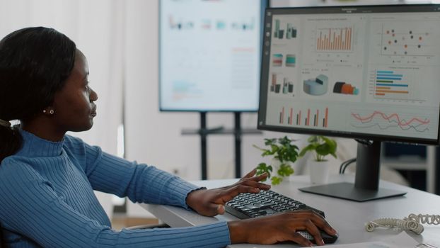 Close up of black paralyzed disabled handicapped woman entrepreneur typing on computer showing data prosessing on desktop checking graphs, financial documents, reading raports in business office