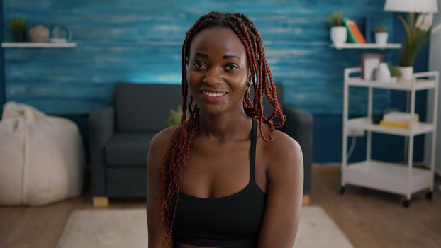 Portrait of fit woman smiling and looking into camera during aerobic morning workout sitting on yoga ball in living room. Athlete adult stretching muscle practicing sport training body muscle