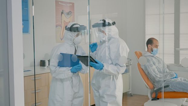Team of dentists with ppe suits holding tablet for teeth consultation at dental clinic. Orthodontists wearing coverall, face shield and gloves using digital technology for oral care