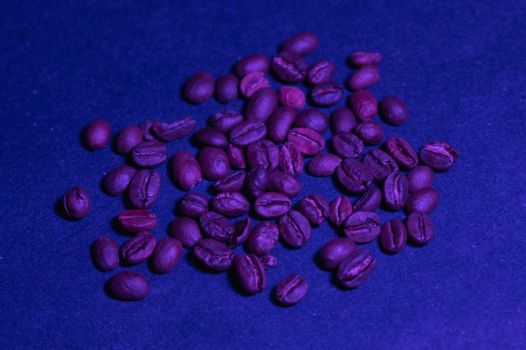 roasted coffee beans are casually scattered on a dark blue background under a blue light on a flat surface
