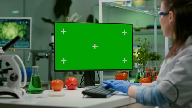 Scientist woman working on computer with mock up green screen chroma key with isolated display observing chemical test. Pharmaceutical researcher working in microbiology laboratory