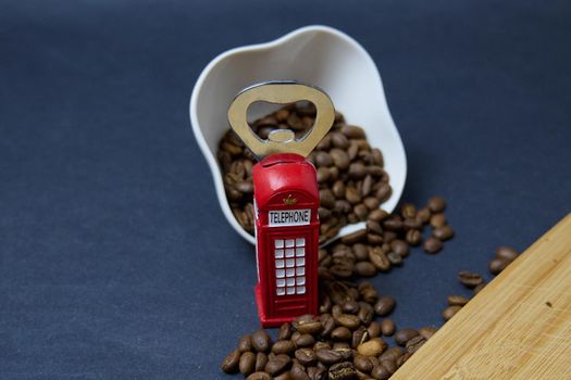 roasted coffee beans on a black background next to a bottle opener in the form of an English telephone booth in red