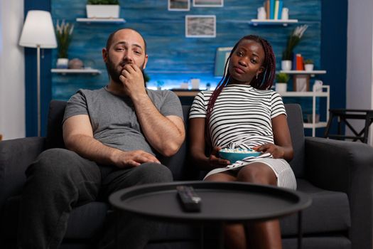 POV of interracial couple watching television enjoying activity in living room. African american woman and caucasian man looking at camera while bonding, relaxing and eating popcorn