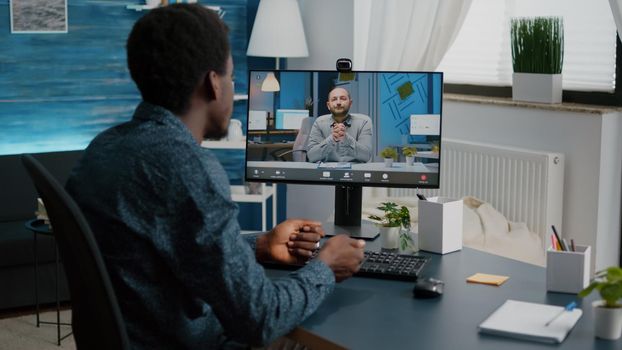 African american man chatting using online web internet communication while working from home office. Remote worker on online video conference with his boss talking via webcam