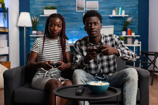 African american couple playing video game on TV console using controllers at television screen in living room. Black married people enjoying modern activity for fun and entertainment