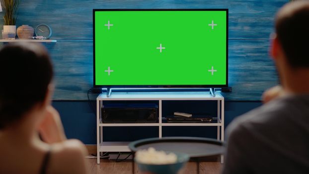 Young adults looking at modern technology green screen on television at home. Caucasian people with copy space and virtual chroma key for isolated template or mockup background