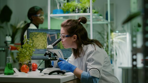 Biologist taking leaf sample putting into microscope observing chemical liquid. Scientist engineering analyzing organic gmo plants while researching in microbiology food laboratory