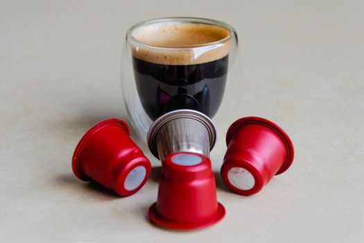 A glass of coffee and capsules for the coffee machine on a wooden table