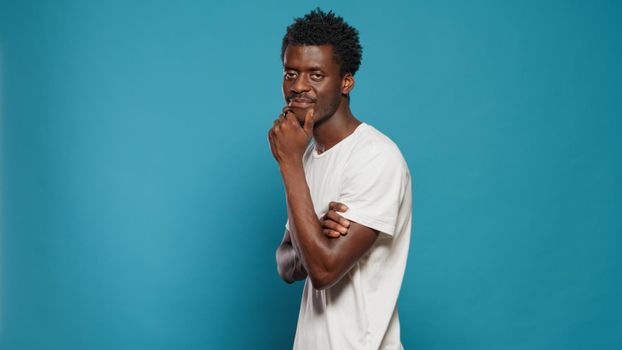 African american man looking at camera and rubbing chin in studio. Black person feeling calm while walking around and having thoughtful expression. Afro posibitive adult with smirk on face
