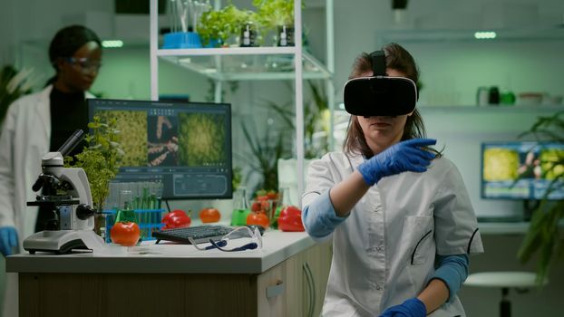 Scientist woman researcher wearing virtual reality headset developing new biotechnology for biological experiment. Medical team working in microbiology laboratory analyzing dna test