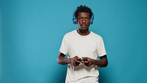 Young man holding joystick to play video games on console. Carefree adult playing online virtual game using controller on television while wearing headphones. Gamer having fun with play
