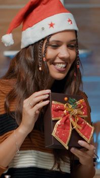 Caucasian person showing wrapped present on video call communication at home. Cheerful woman in festive kitchen using laptop to give gifts to online friends for christmas eve festivity