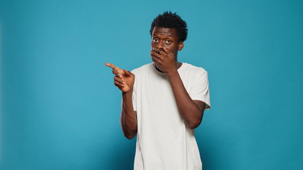 Portrait of person covering mouth with hands after telling secret by mistake. Young man talking about rumour and gossip by accident. Adult ruining surprise and pointing at left side