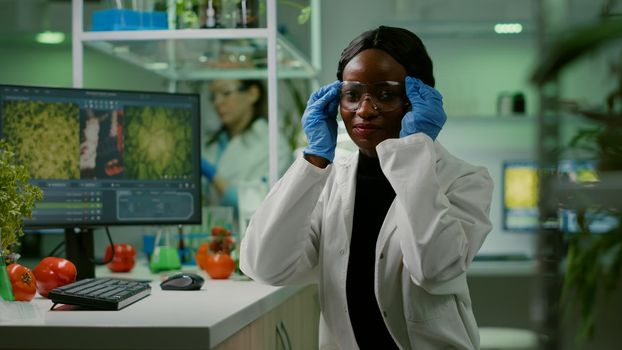 Portrait of african biologist in white coat looking into camera working in microbiology laboratory. Specialists team researching genetic mutation developing dna GMO biology test