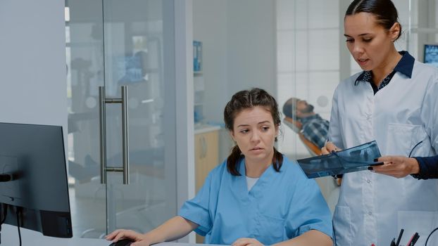 Stomatological team of doctors analyzing dental x ray and computer monitor at orthodontic clinic. Dentist and nurse sitting at desk for operation technique and professional teeth procedure