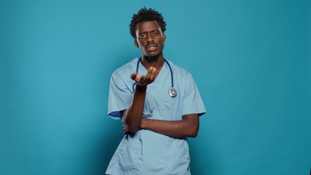 Medical assistant wearing uniform and stethoscope while talking and looking at camera in studio. Man nurse explaining healthcare while standing over isolated background. Health specialist
