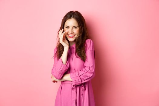 Beauty and fashion. Attractive caucasian woman giggle and smile at camera, posing in romantic bright dress on fine spring day, standing against pink background.