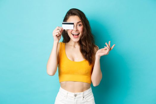 Excited beautiful woman in summer cropped top, look amazed at camera, shopping with credit card, standing over blue background.