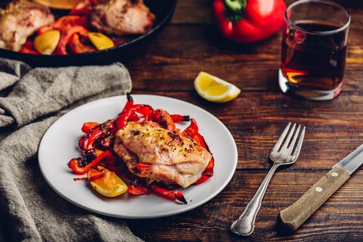 Oven baked chicken thighs with red bell peppers and lemon on white plate.