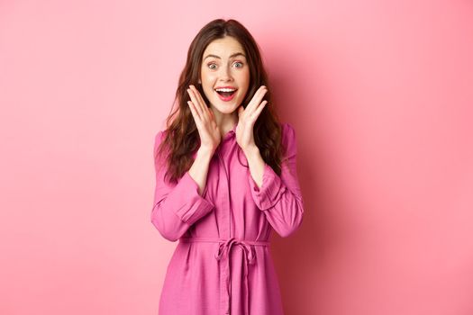 Image of beautiful surprised woman gasping amazed, look at fantastic news, smiling astonished, standing over pink background.