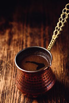 Turkish coffee. Brewed coffee in copper cezve on wooden surface