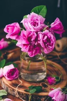 Bouquet of small pink garden roses in jar on wooden table
